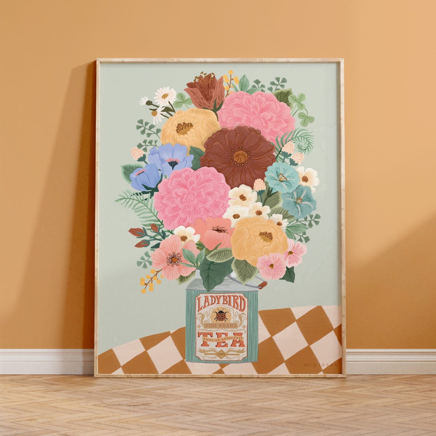 Photo showing our boho floral vase art print, in a light wood frame, leaning against a mustard wall. Our boho floral art print consists of a bunch of flowers and foliage in a vintage square ladybird tea bottle on a table with a checked tablecloth on a light green background. The flowers are of varying types and come in shades of red, pink, purple, blue, yellow and cream. 