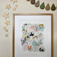Our Crayon Wilderness art print in a dark oak frame hung on a neutral wall, with rain drop bunting in autumnal hues, and wooden stars framing the hung art work. Our Crayon Wilderness Art print is hand-drawn with floral details in greens and pinks, with pop of brighter colours, with animals featuring pandas, swans, foxes, deer and raccoons, creating a whimsical woodland feel.
