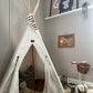 A cream Nobodinoz teepee, set up with blankets and cushions inside, with a cream triangle flag with EXPLORE in brown hanging from the top, with a black lantern, wellies, and a Banwood scooter next to it. On the wall, in an oak hanger is our forever fearless art print, and above that on a white shelf is our G is for gorilla art print and a hanging succulent.